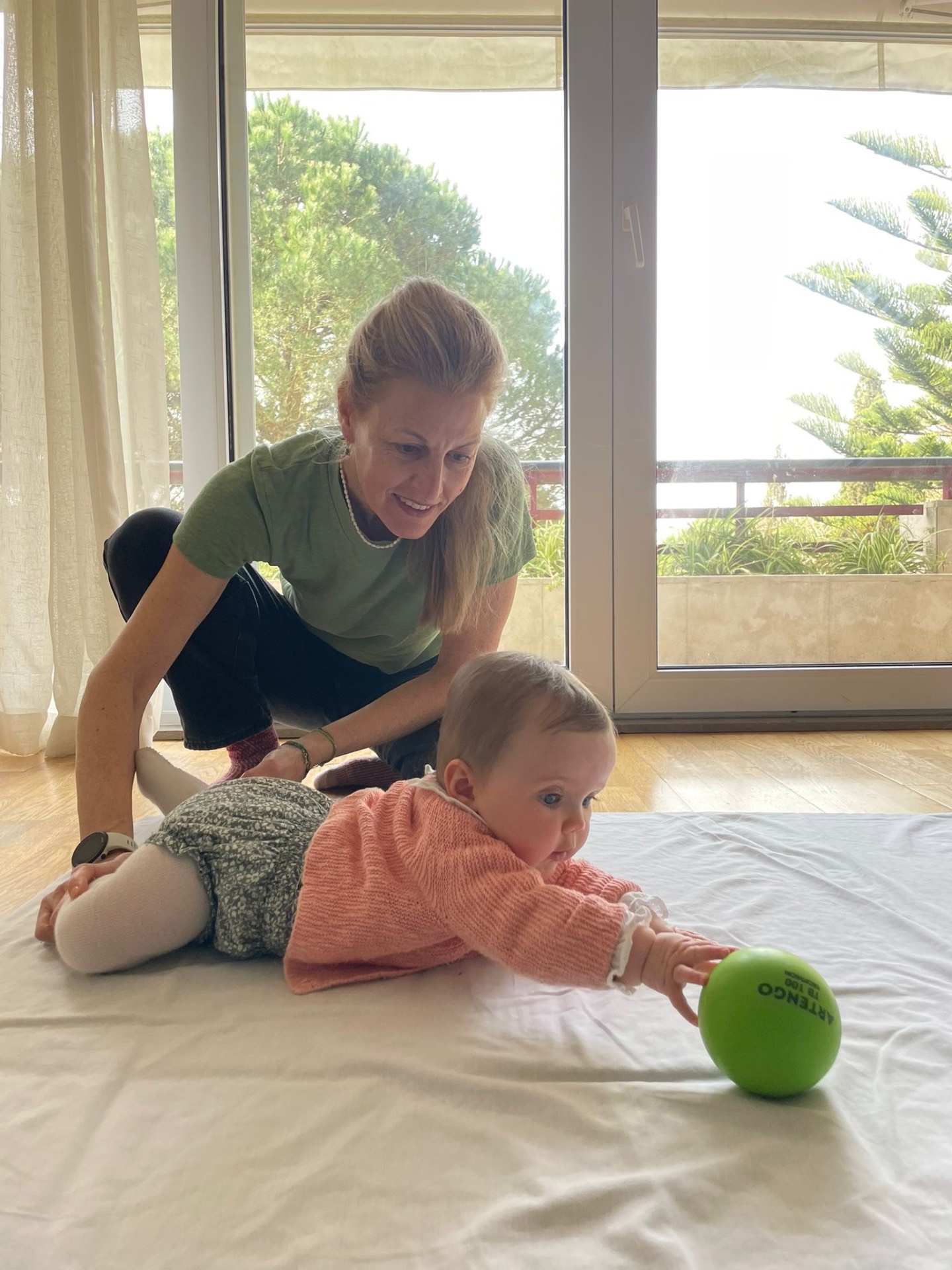 Naomi supporting an infant reaching for a green ball during a developmental session